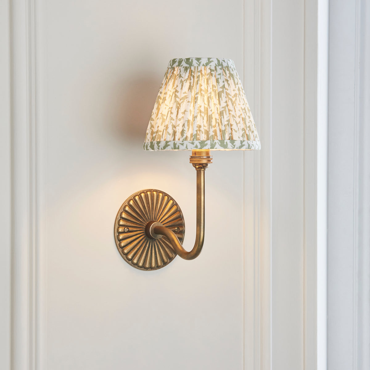 Angled view of the Dahlia Swan brass swan-neck wall light with green foliage-print pleated shade