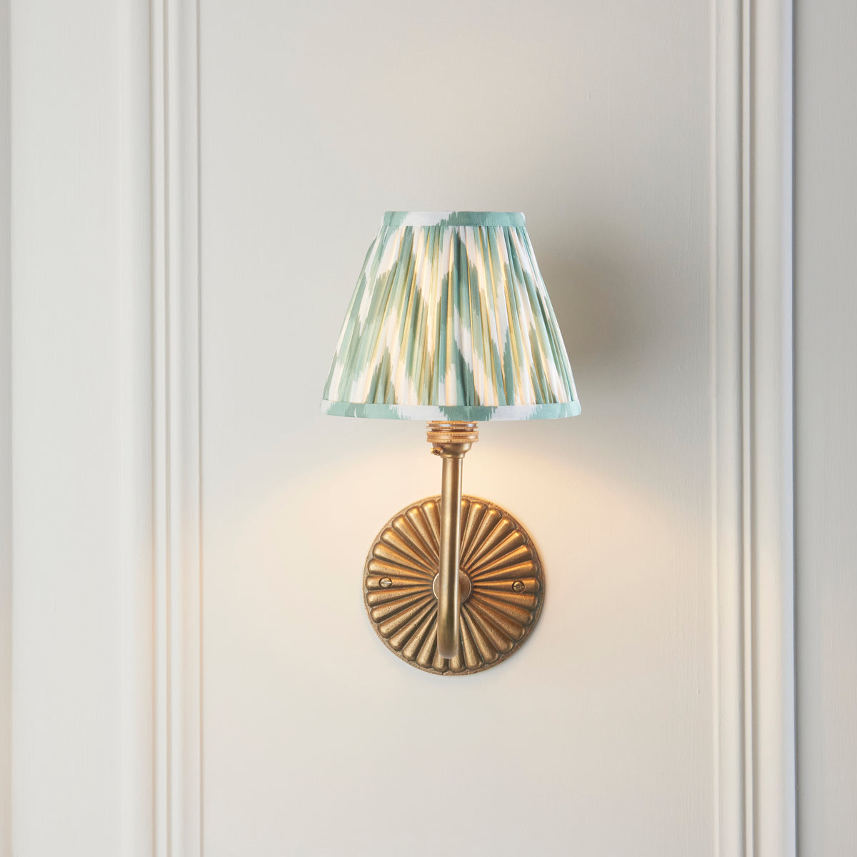 Front view of the Dahlia Swan wall light with fluted brass backplate and green ikat pleated shade