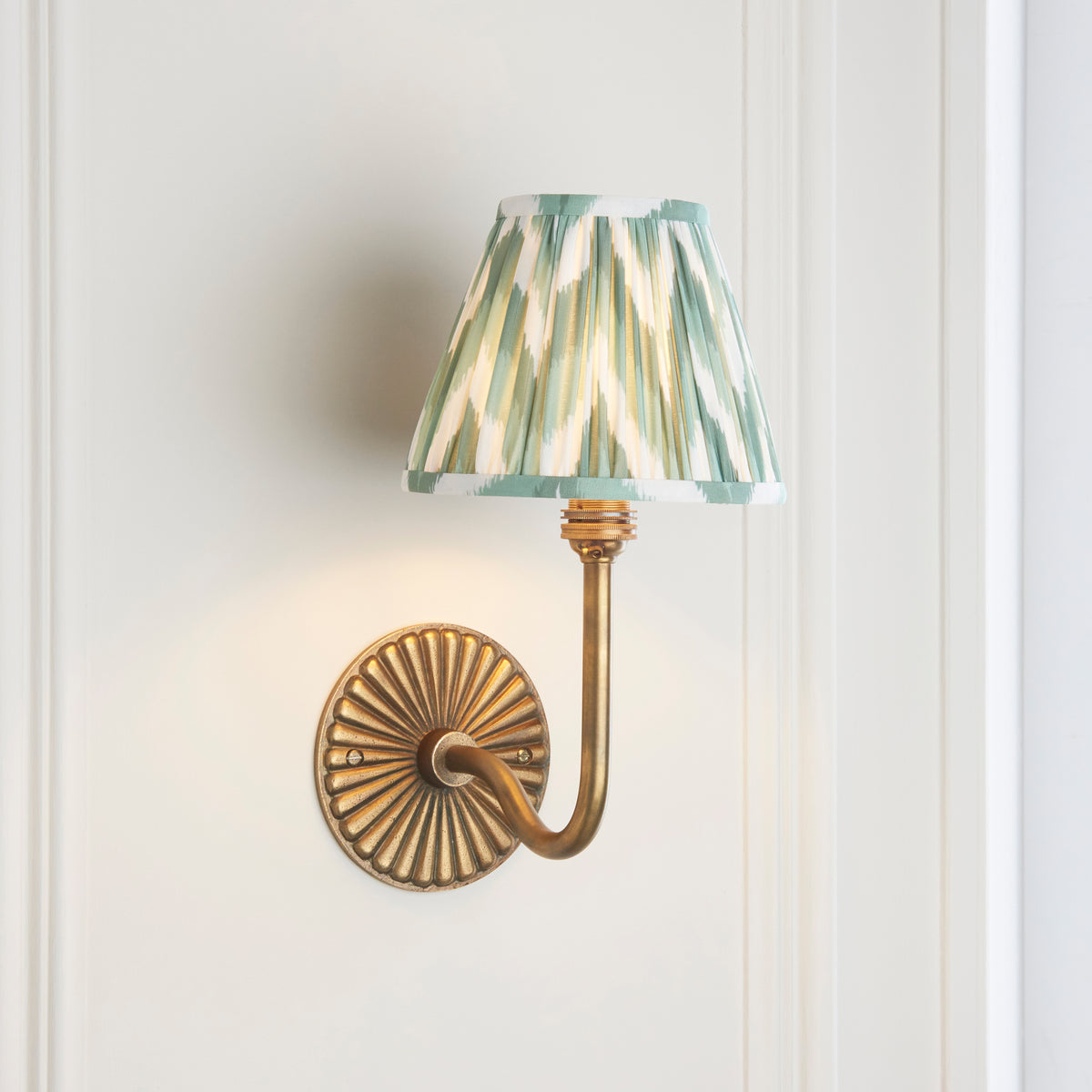 Angled view of the swan-neck brass wall light with green and cream zigzag ikat pleated shade