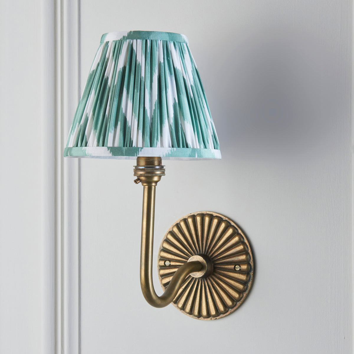 Dahlia Swan antique brass wall light on grey wall, soft green zigzag ikat pleated shade