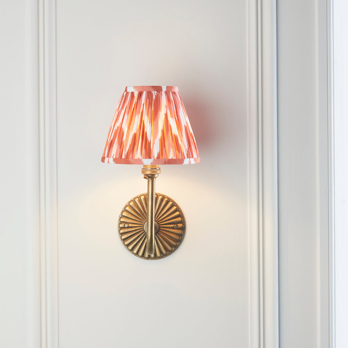 Front view of the Dahlia Swan wall light, fluted brass backplate and coral ikat pleated shade