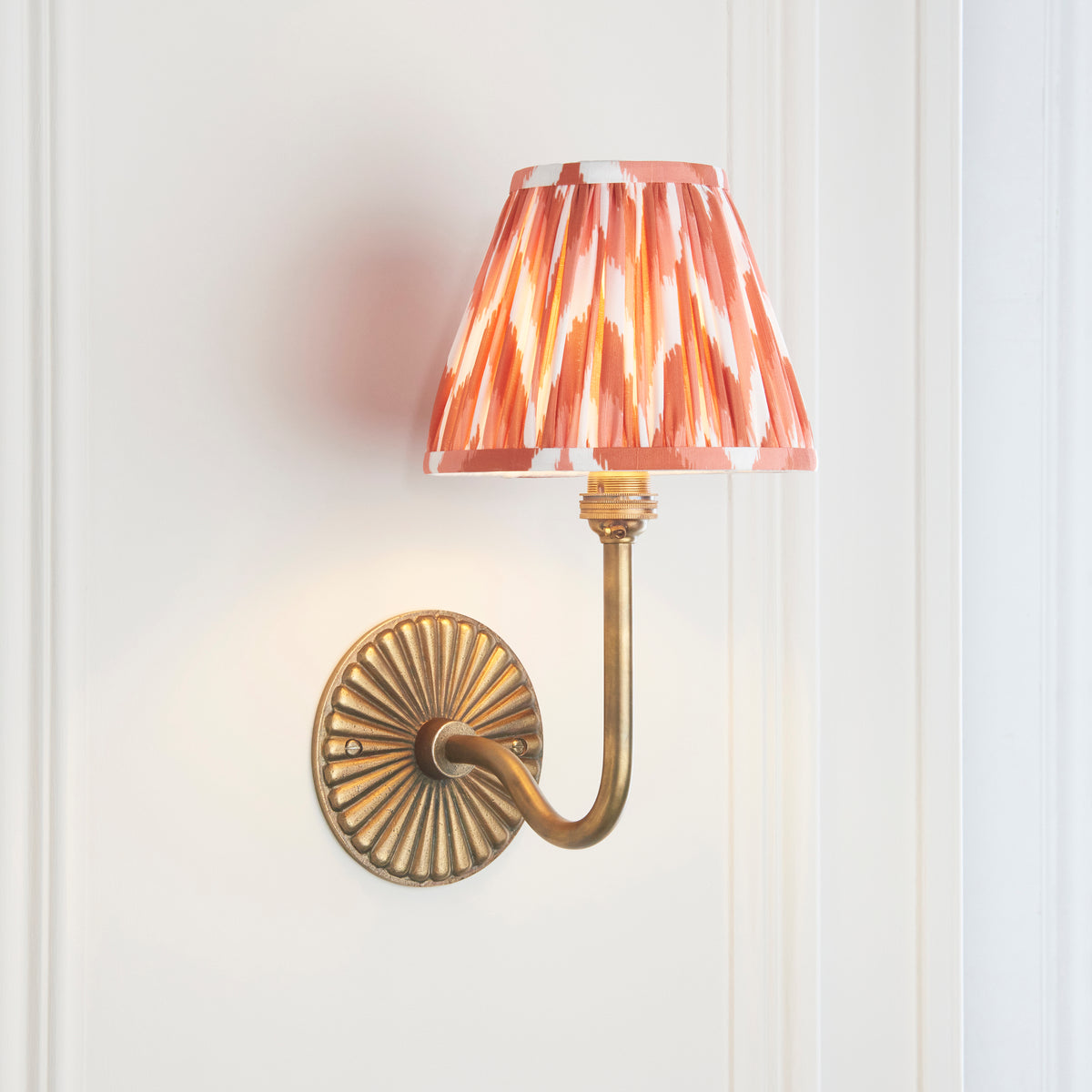Angled view of the swan-neck brass wall light with orange and cream zigzag ikat pleated shade