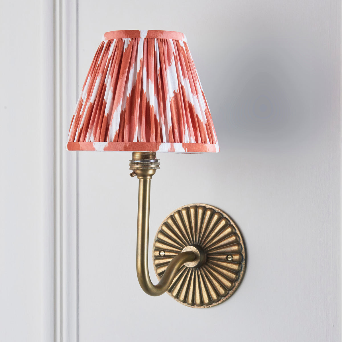 Dahlia Swan antique brass wall light on grey wall with terracotta zigzag ikat pleated shade