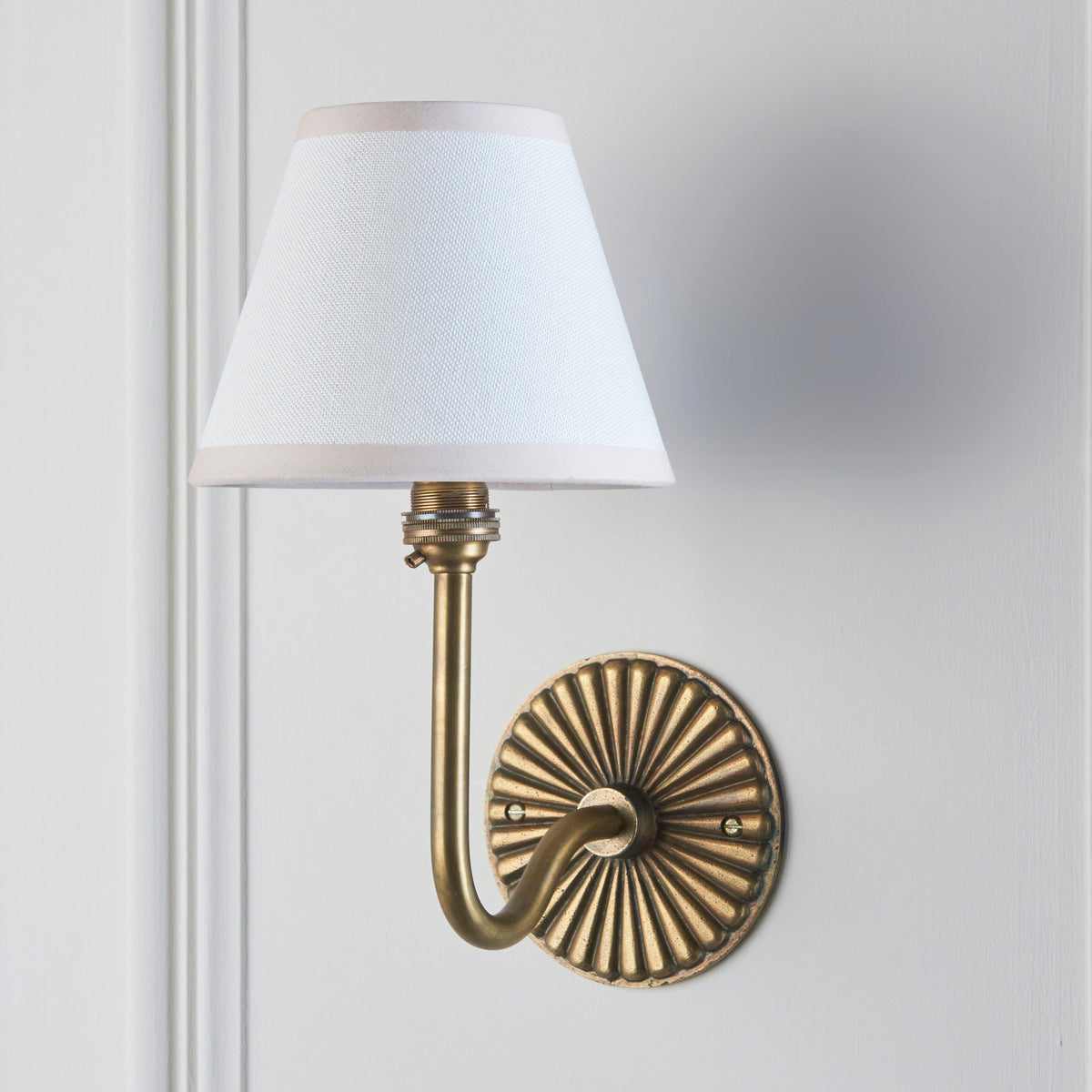 Dahlia Swan antique brass wall light on grey wall with crisp white linen tapered shade