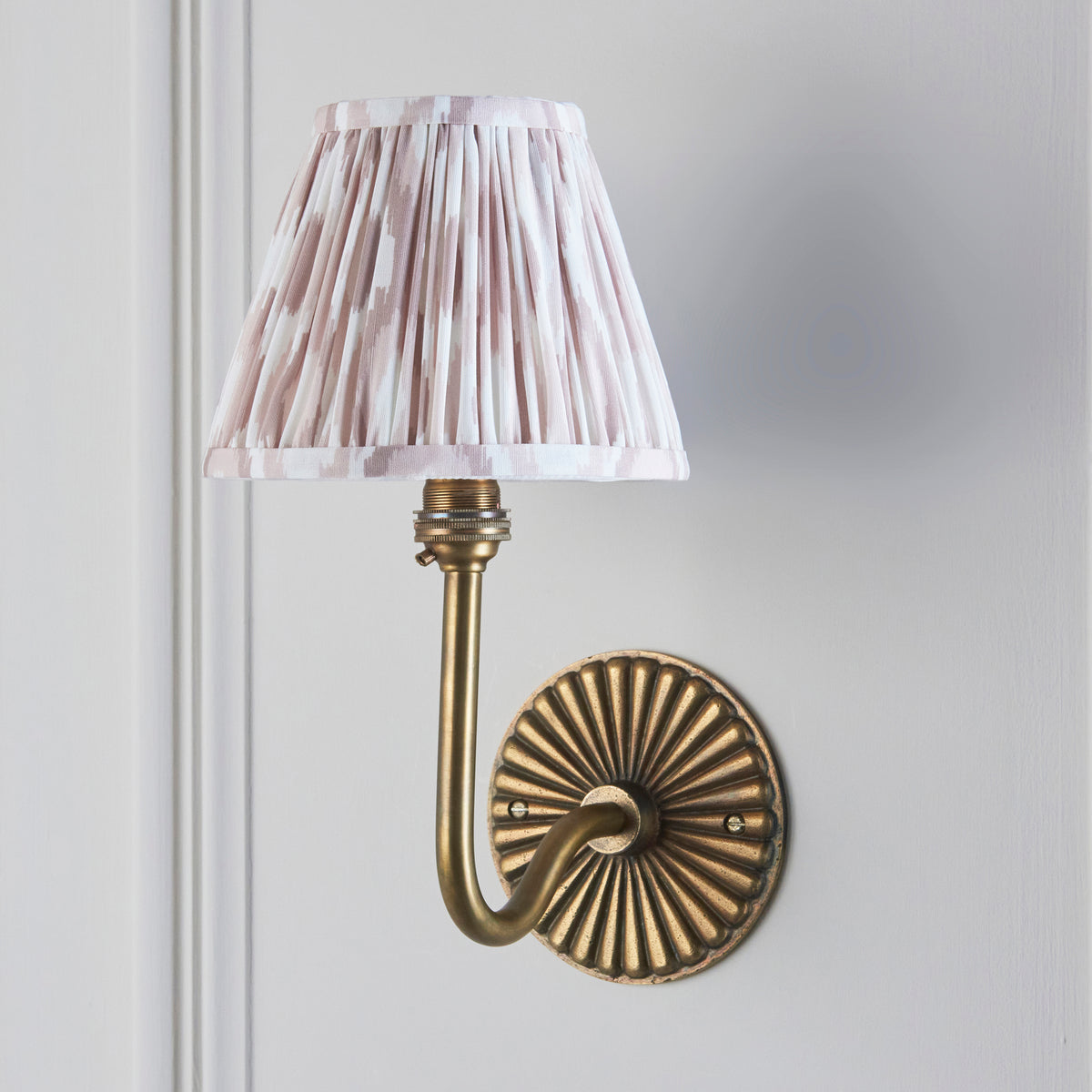 Dahlia Swan antique brass wall light on grey wall with neutral ikat pleated tapered shade