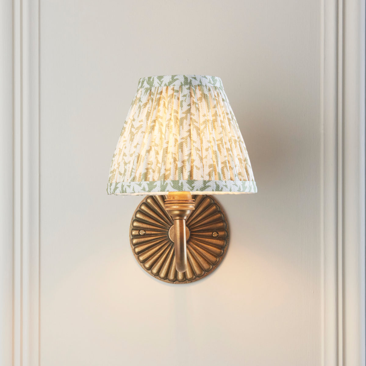 Front view of the Dahlia Curve wall light, fluted brass backplate and green leaf pleated shade
