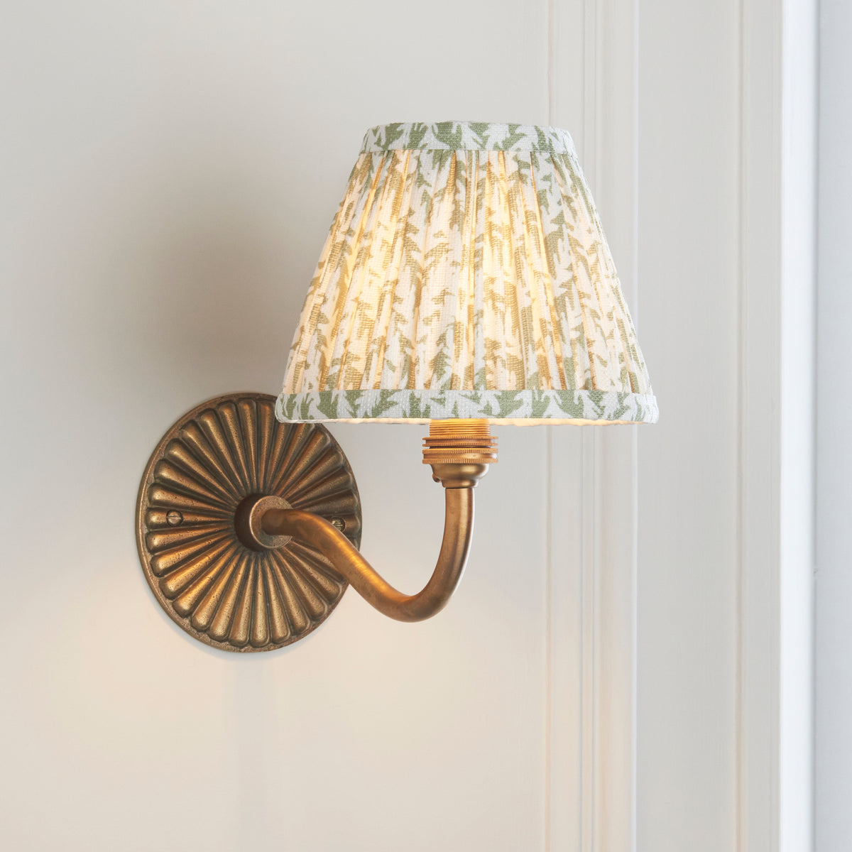 Angled view of the Dahlia Curve brass wall light with green foliage-print pleated shade