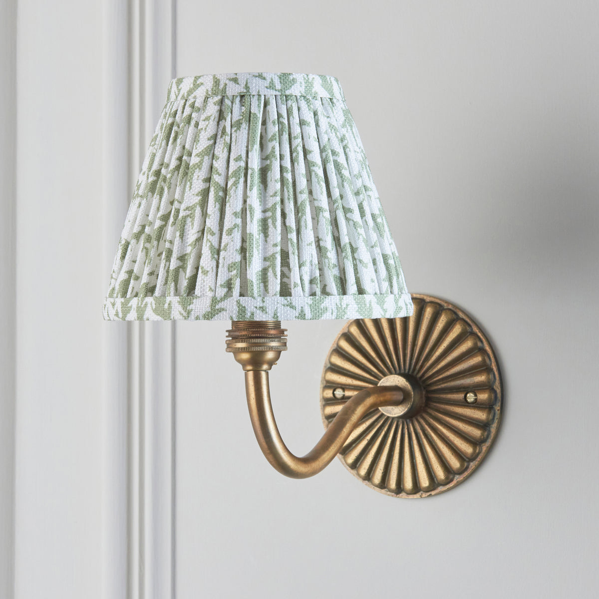 Dahlia Curve antique brass wall light on grey panelled wall with green leaf pleated shade