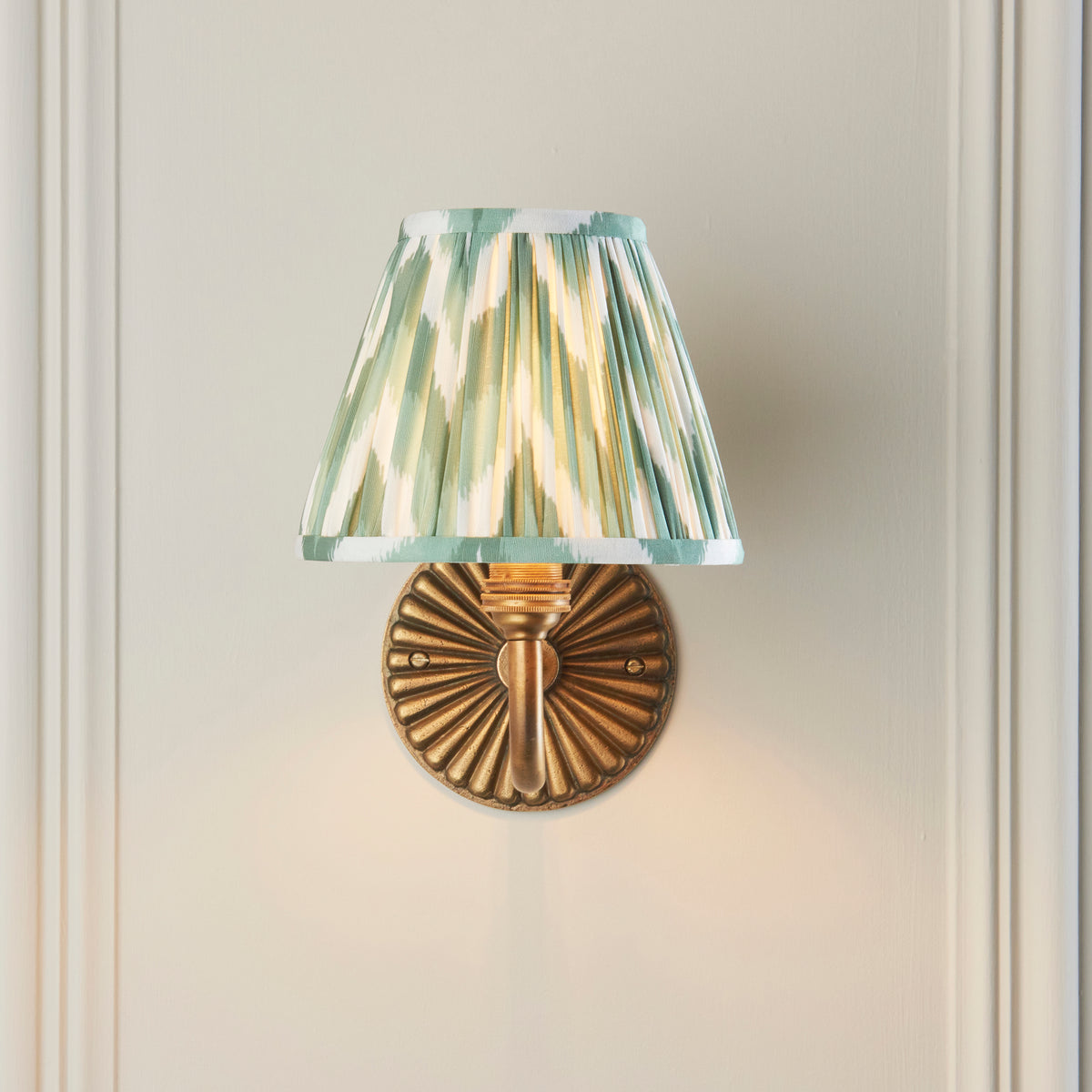 Front view of the Dahlia Curve wall light with fluted brass backplate and green ikat shade