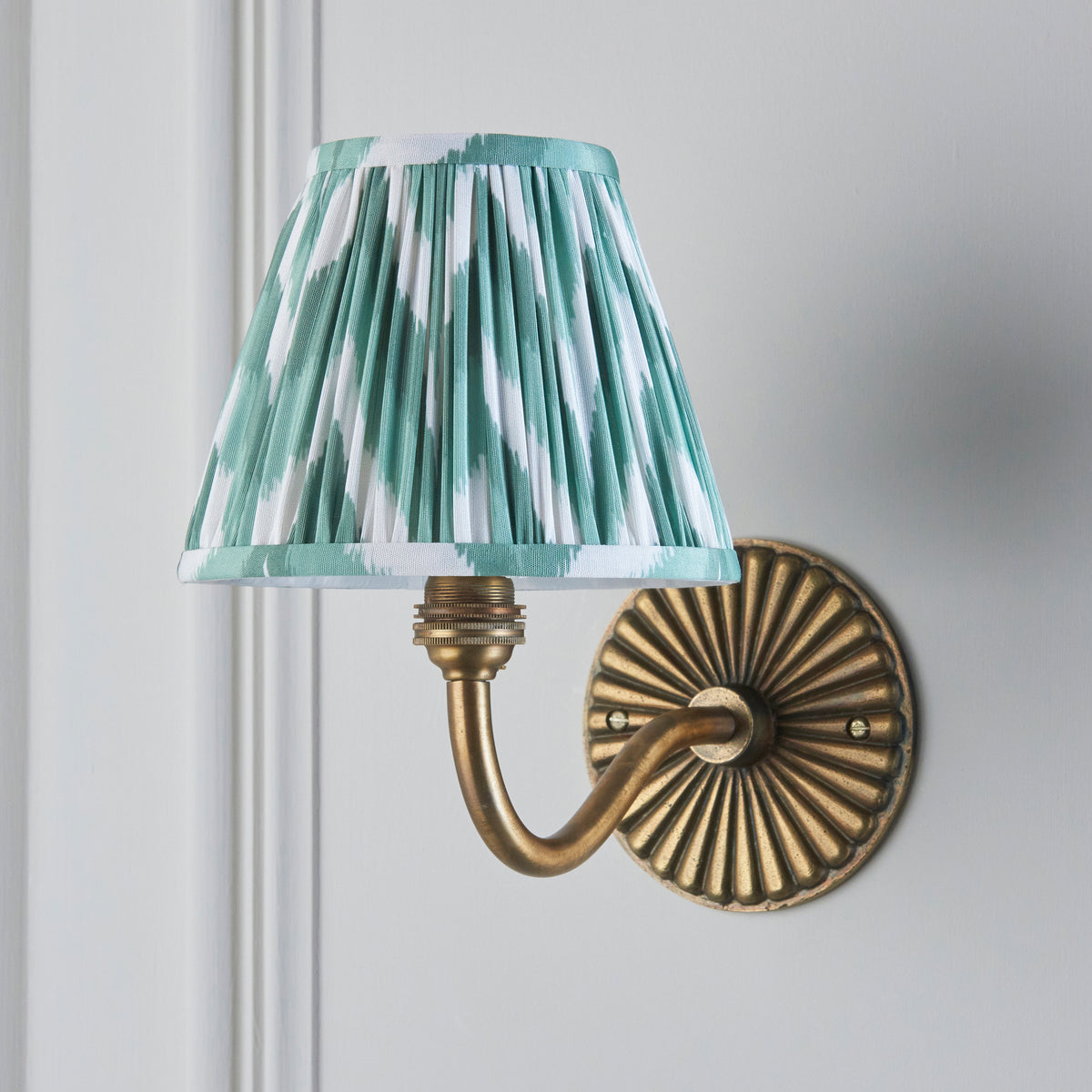Dahlia Curve antique brass wall light on grey panelled wall with green ikat pleated shade
