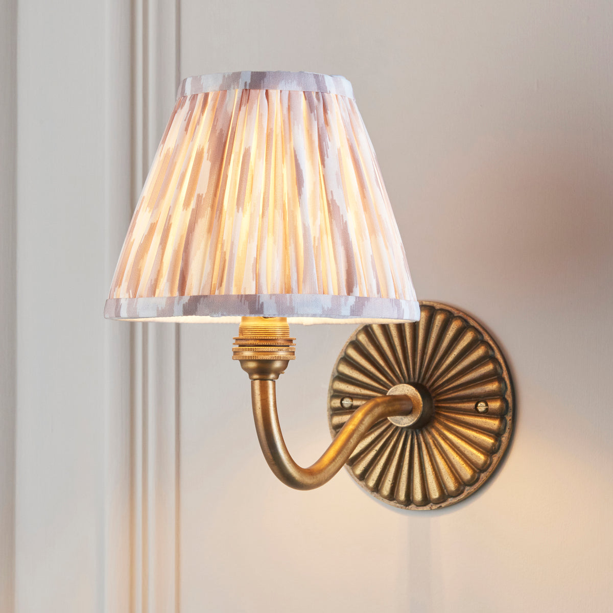 Natural ikat pleated shade glowing on the Dahlia Curve brass wall light against panelled walls