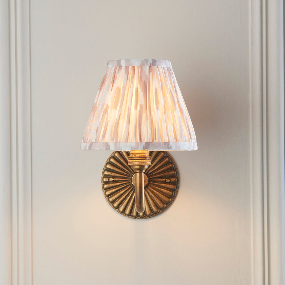 Front view of the Dahlia Curve sconce, fluted brass backplate beneath a neutral ikat pleated shade