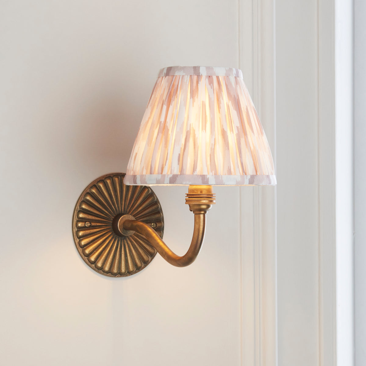 Angled view of the antique brass Dahlia Curve wall light with warm-lit natural ikat shade