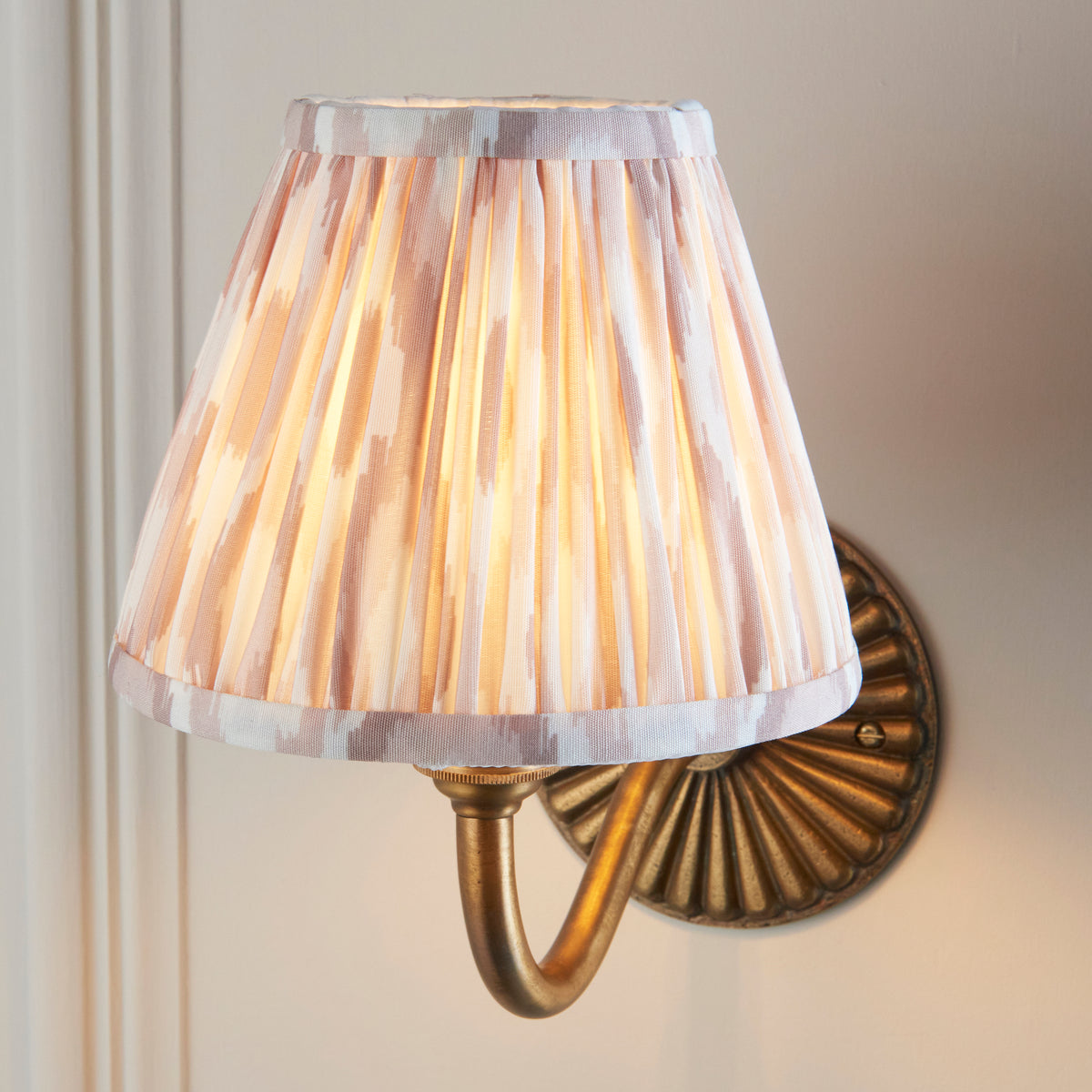 Close view of the illuminated beige and cream pleated ikat shade on the curved brass sconce