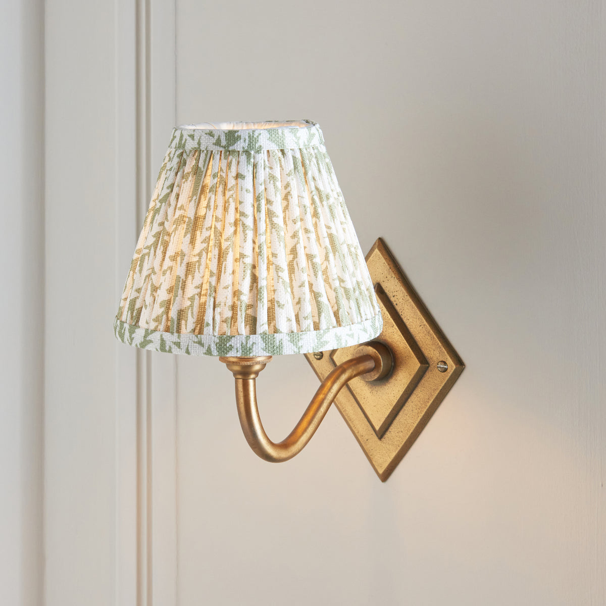 Close view of the pleated green leaf shade above the curved brass arm and diamond backplate