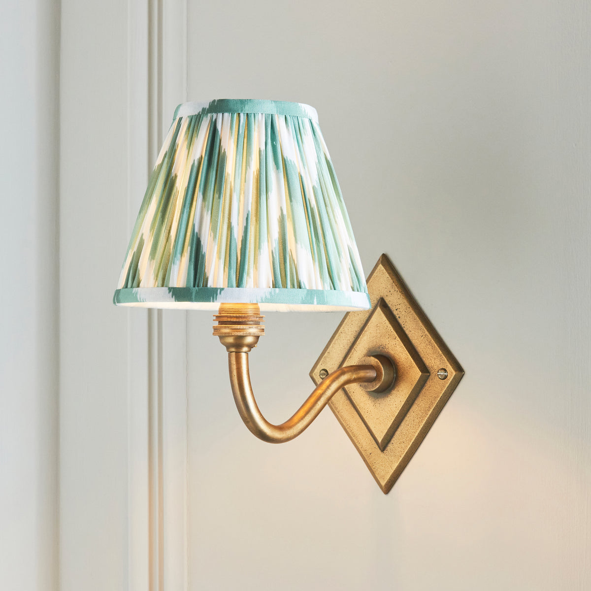 Green zigzag ikat shade lit on the Diamond Curve brass wall light against pale wall panelling