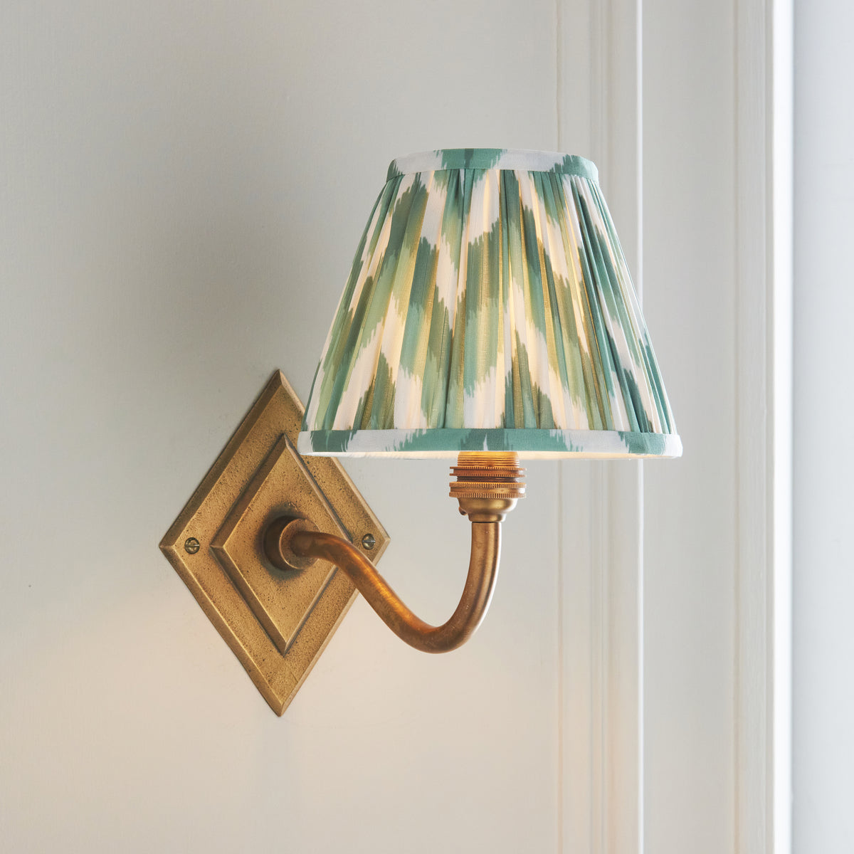 Angled view of the Diamond Curve brass wall light with warm-lit green and cream zigzag shade
