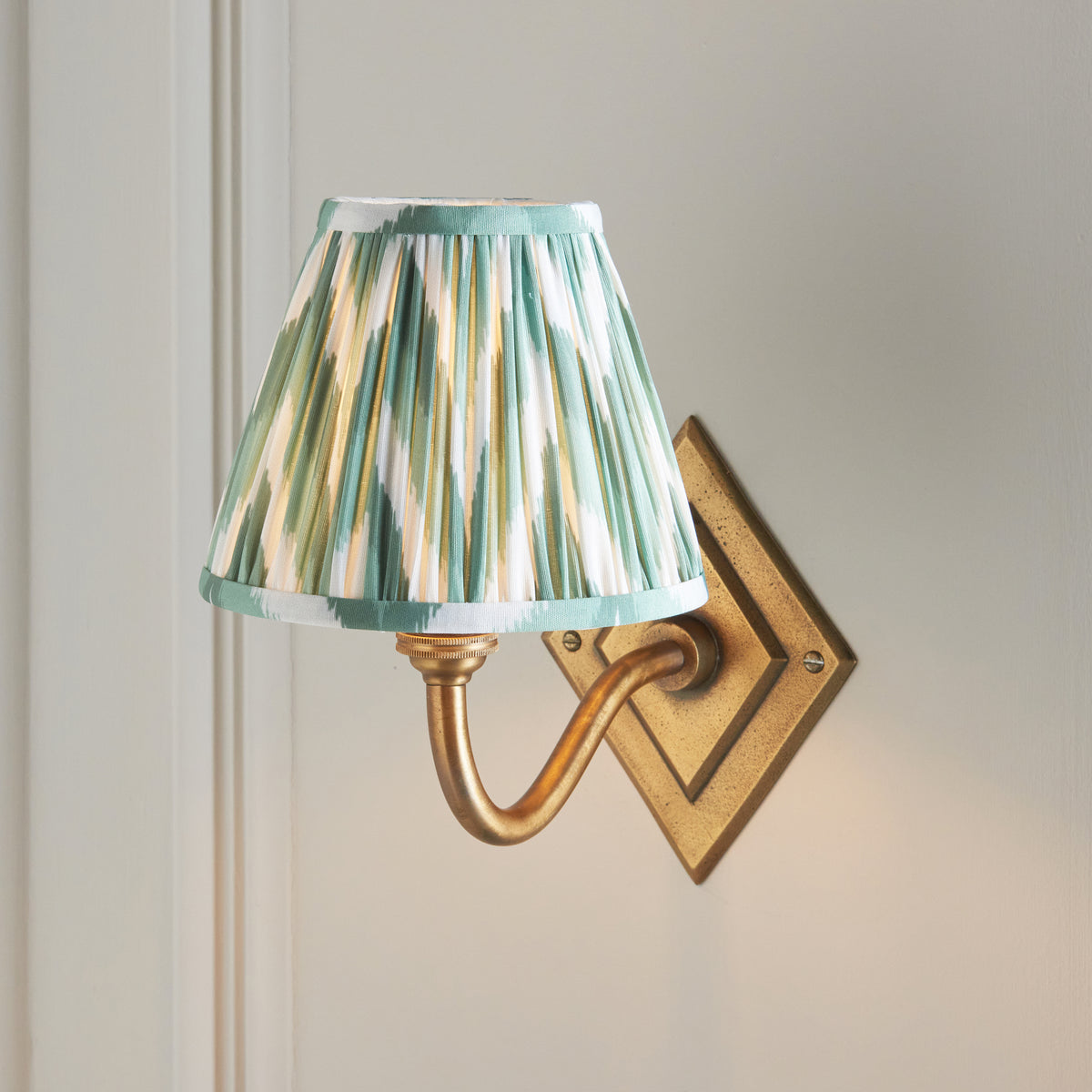 Close view of the pleated green ikat shade above the curved brass arm of the Diamond Curve light