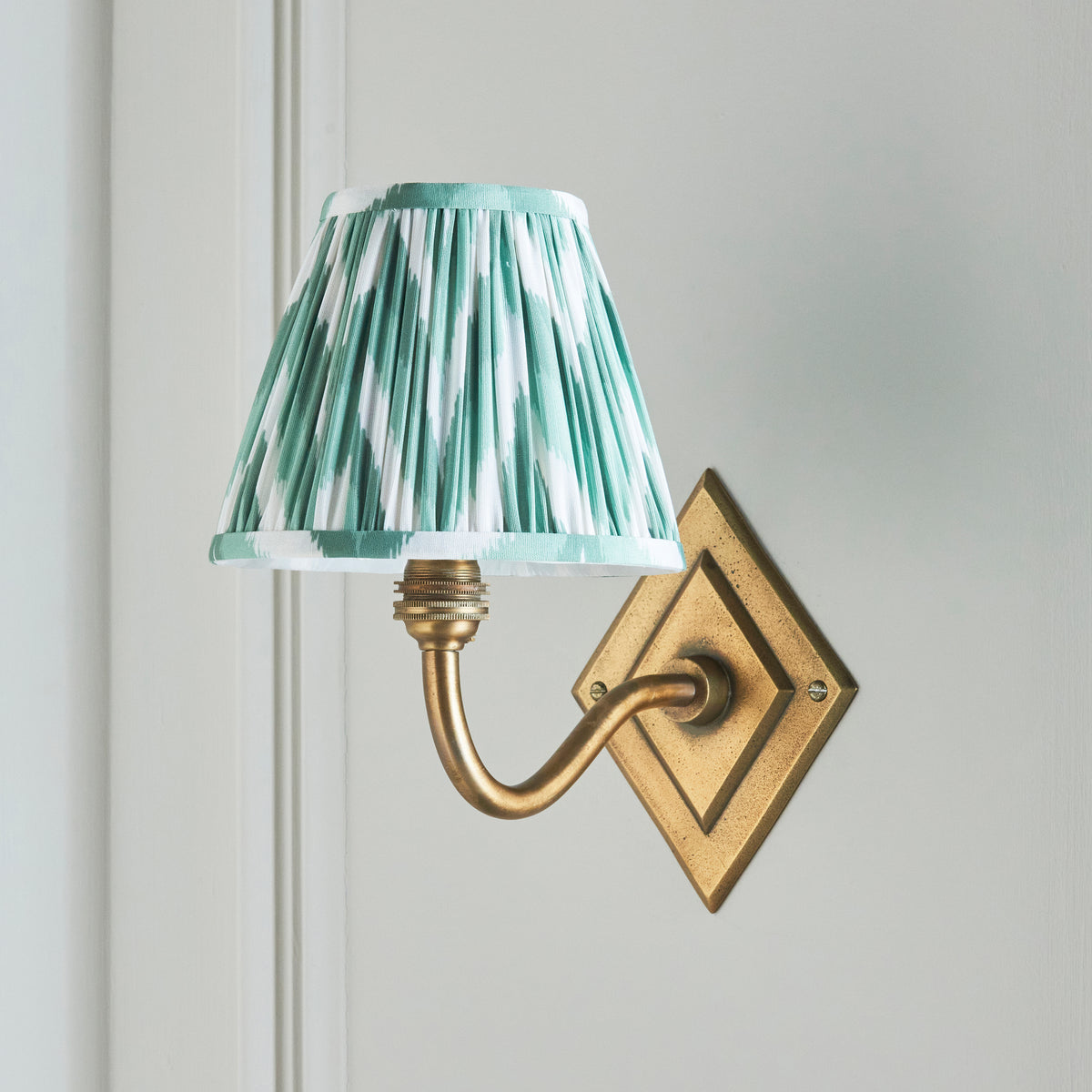 Side view of the Diamond Curve wall light, green zigzag shade and antique brass diamond backplate