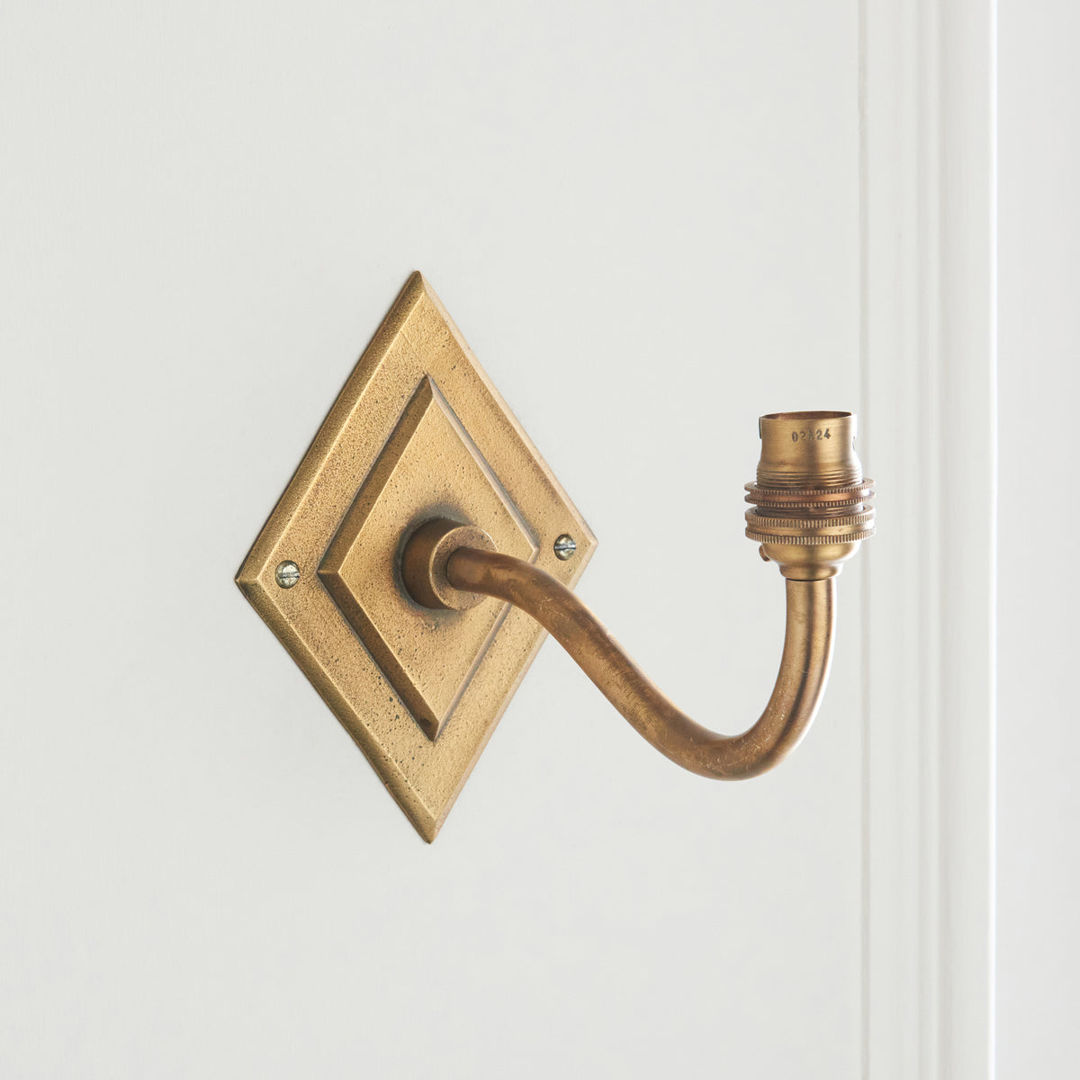 Detail of the diamond brass backplate, curved arm and exposed lamp holder of the sconce