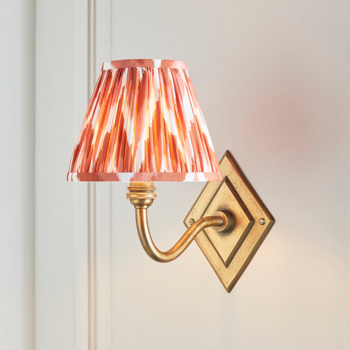 Orange zigzag ikat shade glowing on the Diamond Curve brass wall light against pale panelling