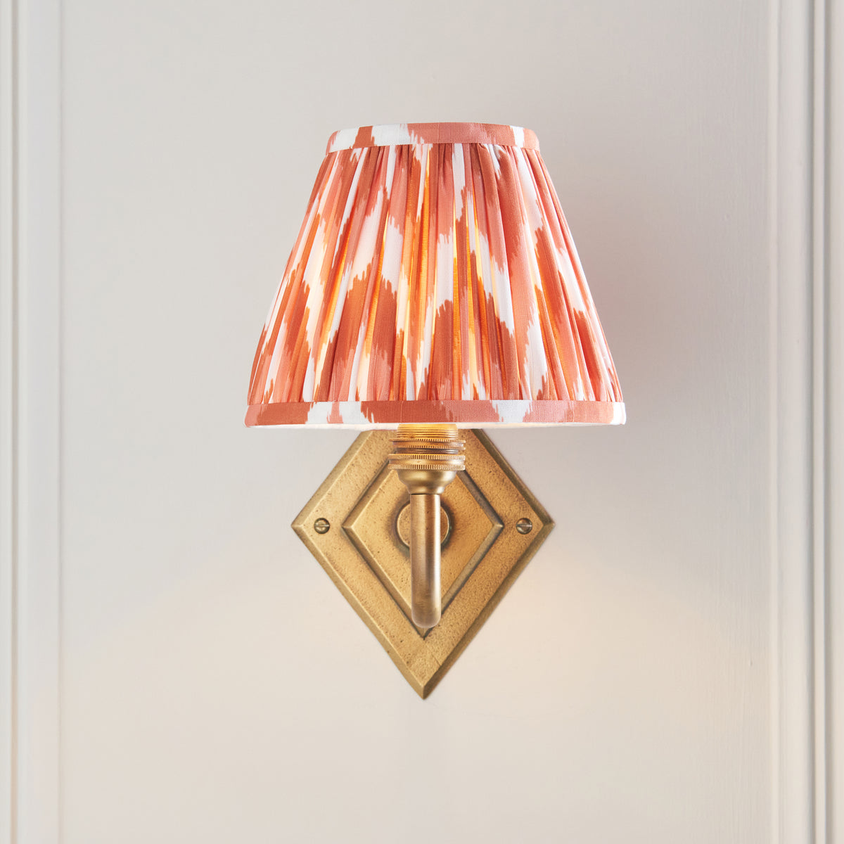 Front view of the Diamond Curve sconce, brass diamond backplate beneath a lit orange ikat shade