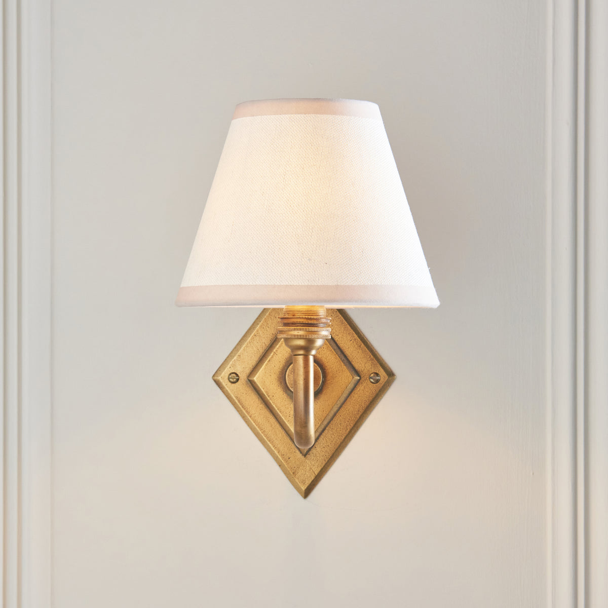 Front view of the Diamond Curve sconce, brass diamond backplate below a plain ivory shade