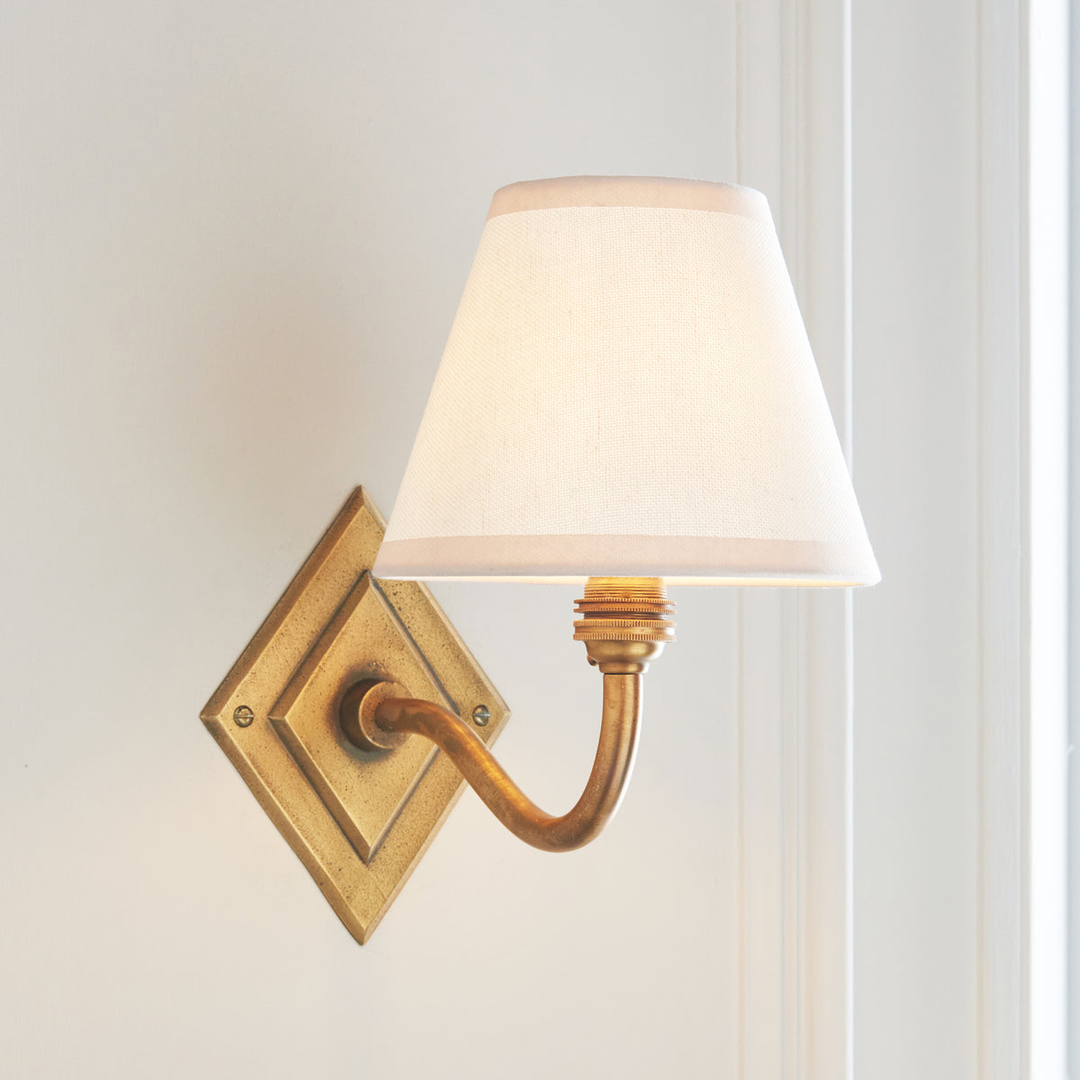Angled view of the Diamond Curve brass wall light with softly glowing white fabric shade