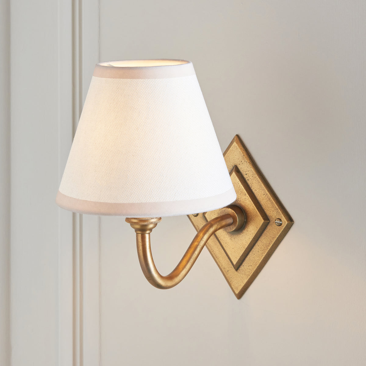 Close view of the tapered white shade on the curved antique brass arm of the Diamond Curve light