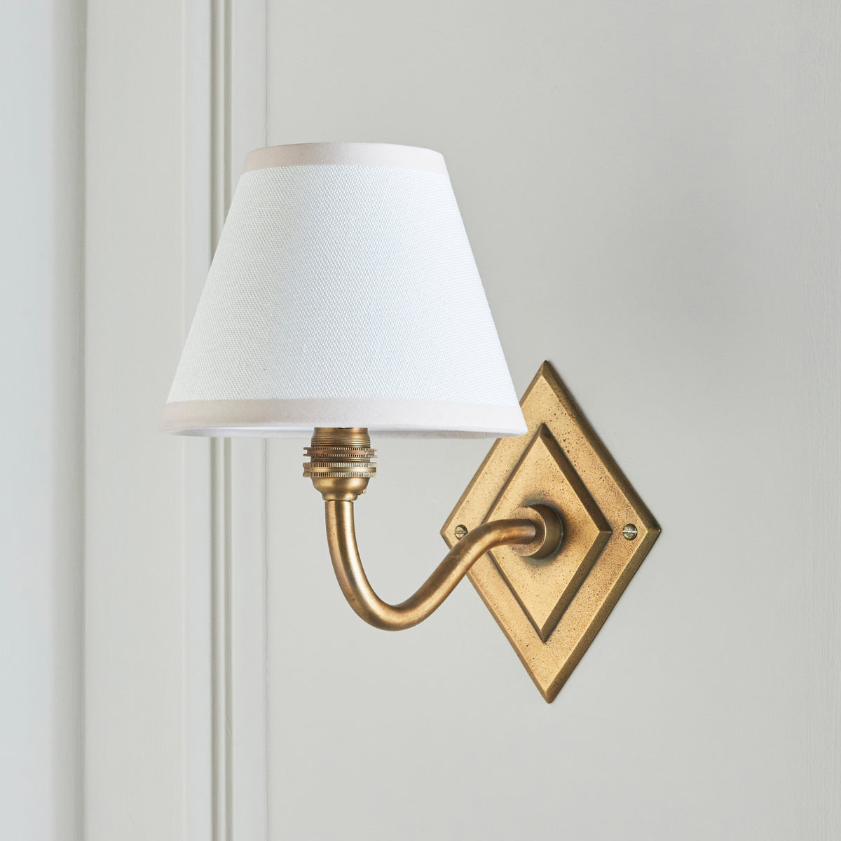 Side view of the Diamond Curve wall light, crisp white shade and antique brass diamond backplate