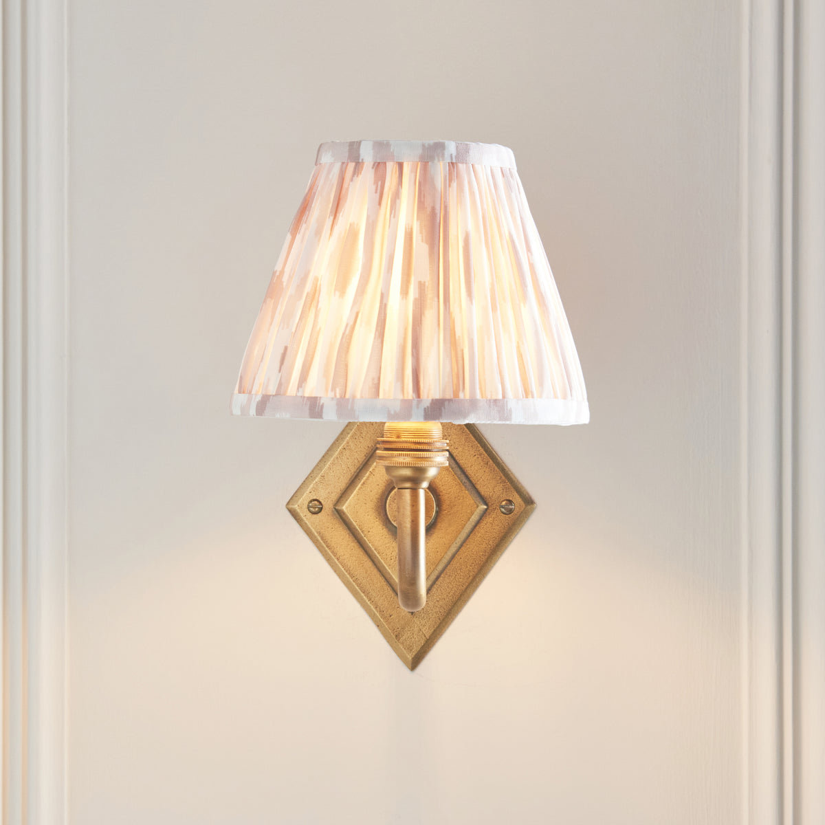 Front view of the Diamond Curve sconce, brass diamond backplate under a neutral ikat pleated shade