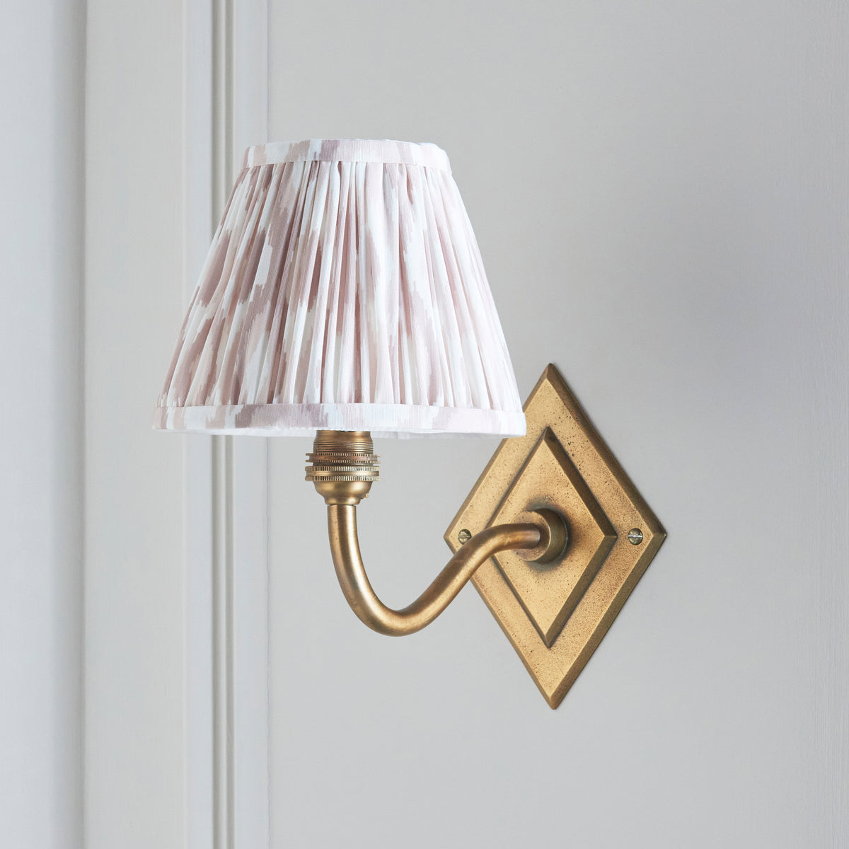 Side view of the Diamond Curve wall light, soft neutral ikat shade against cream panelling