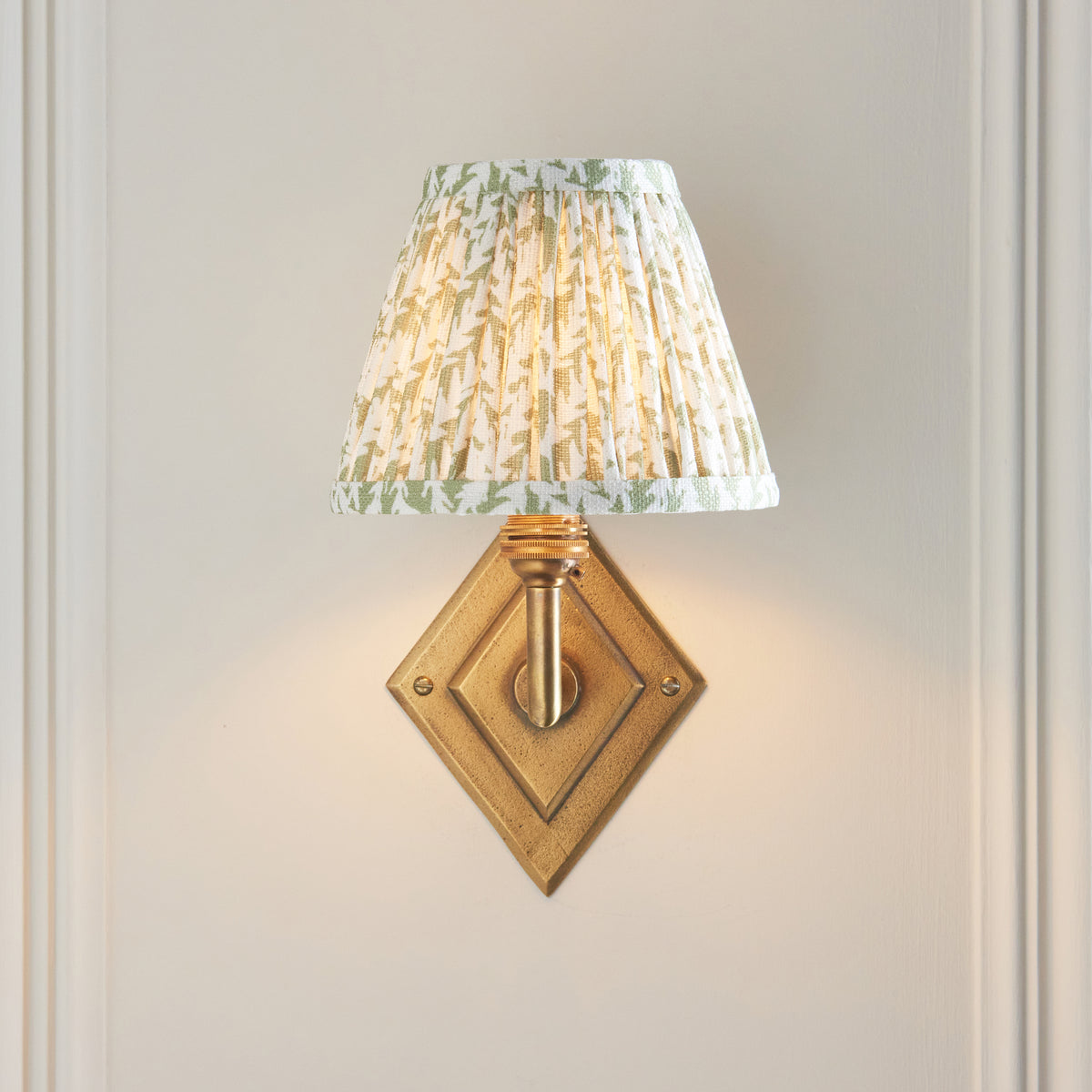 Diamond Angle wall light lit against white panelling, showing the diamond brass backplate head-on