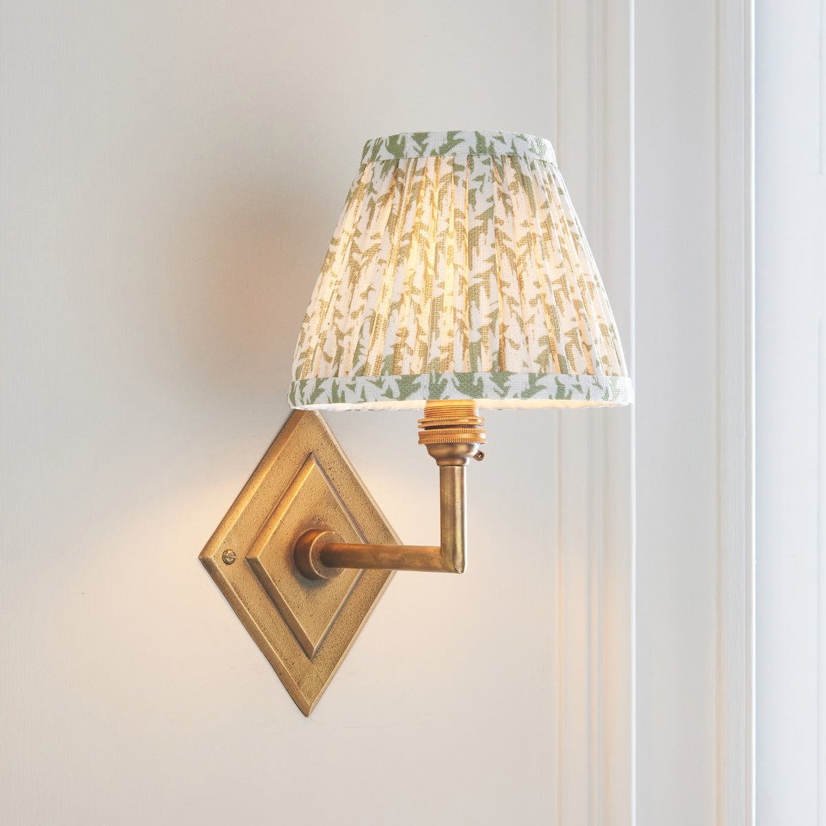 Lit Diamond Angle brass wall light casting a warm glow on a white panelled wall
