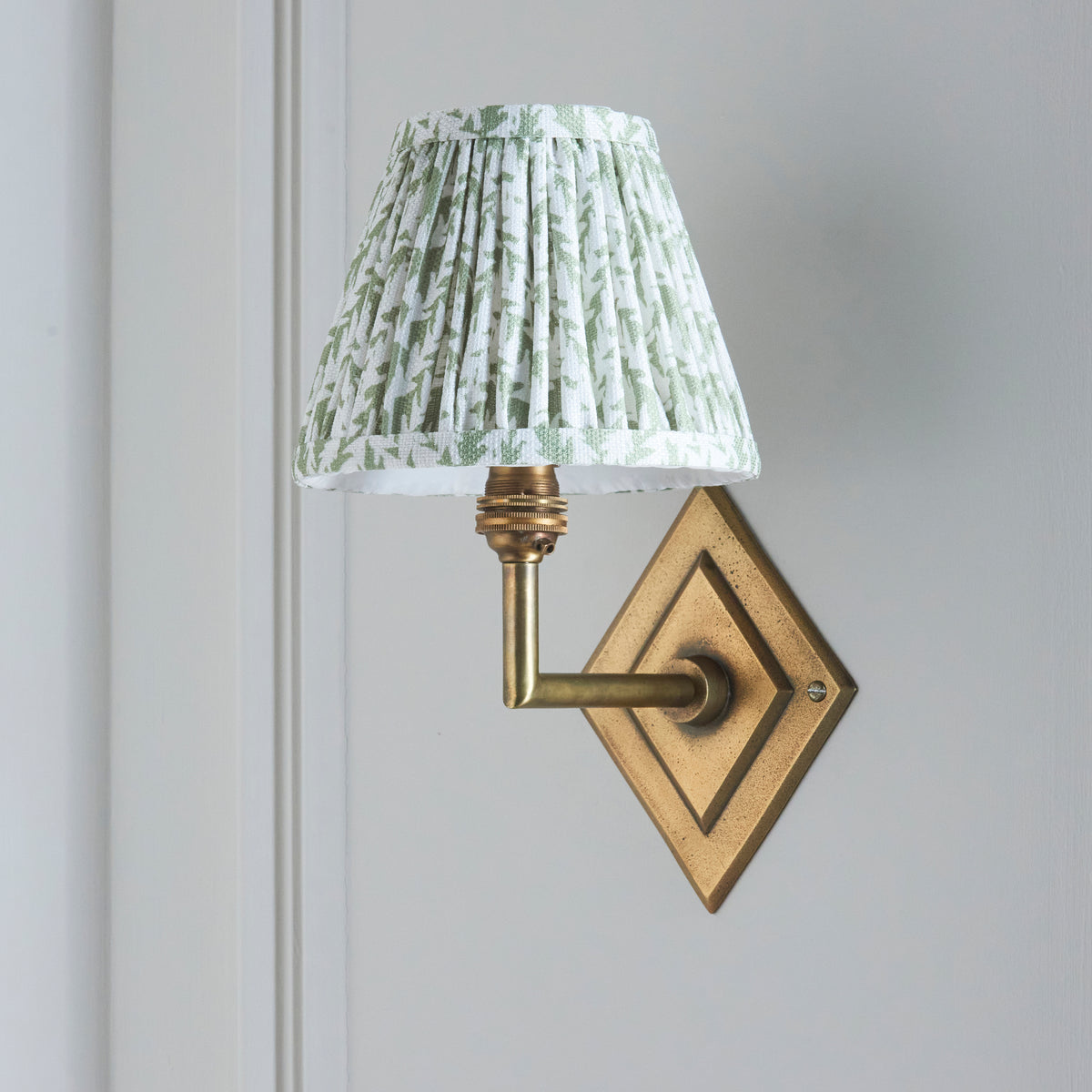 Diamond Angle brass wall light seen from the side, leaf-print pleated shade unlit