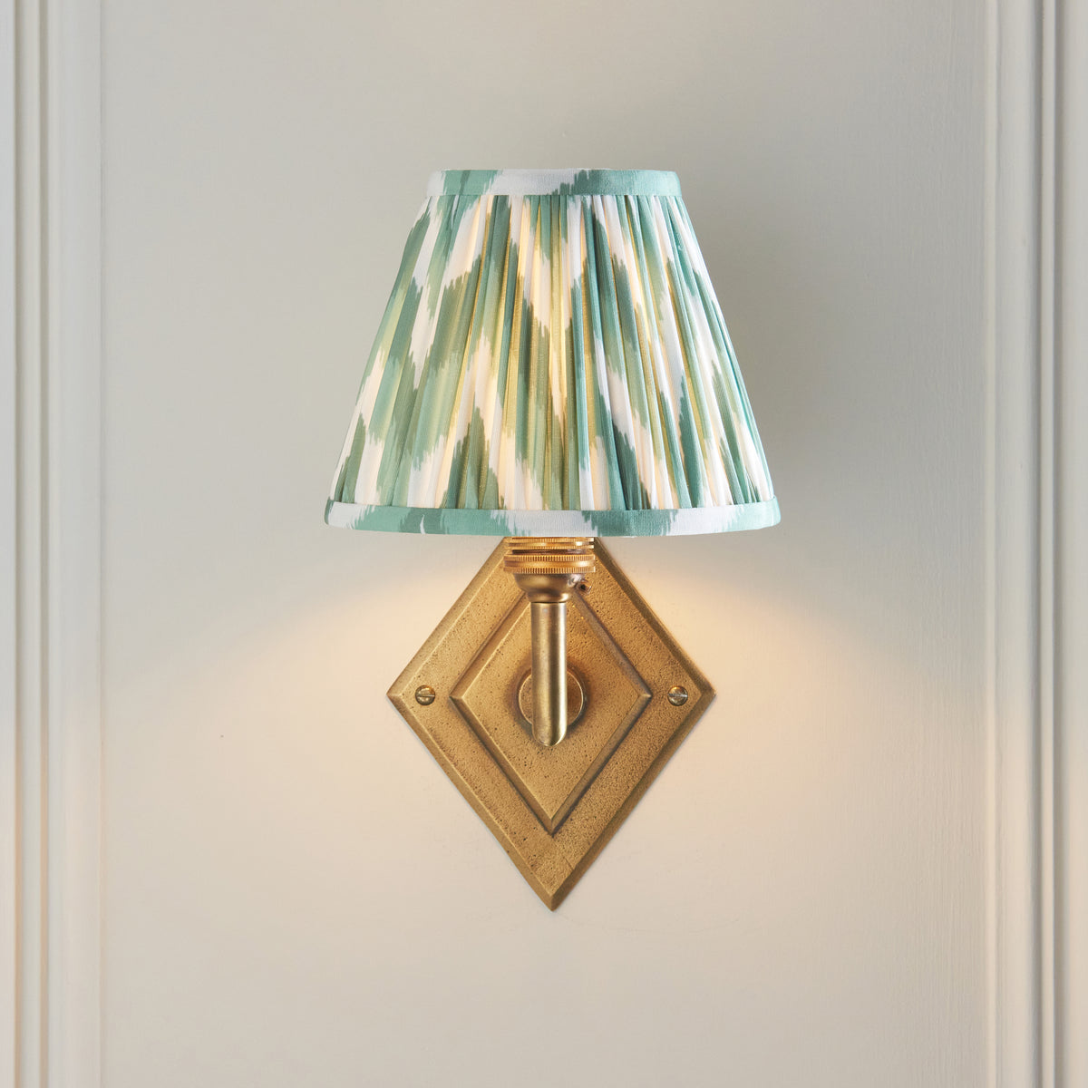 Lit Diamond Angle wall light shown head-on, diamond brass backplate and green ikat shade
