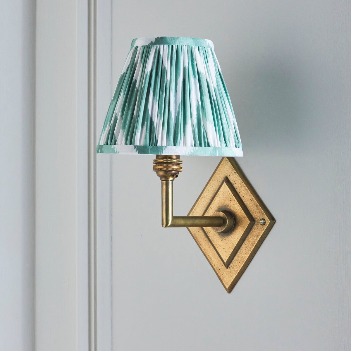 Side view of the Diamond Angle brass wall light with its green zigzag ikat pleated shade