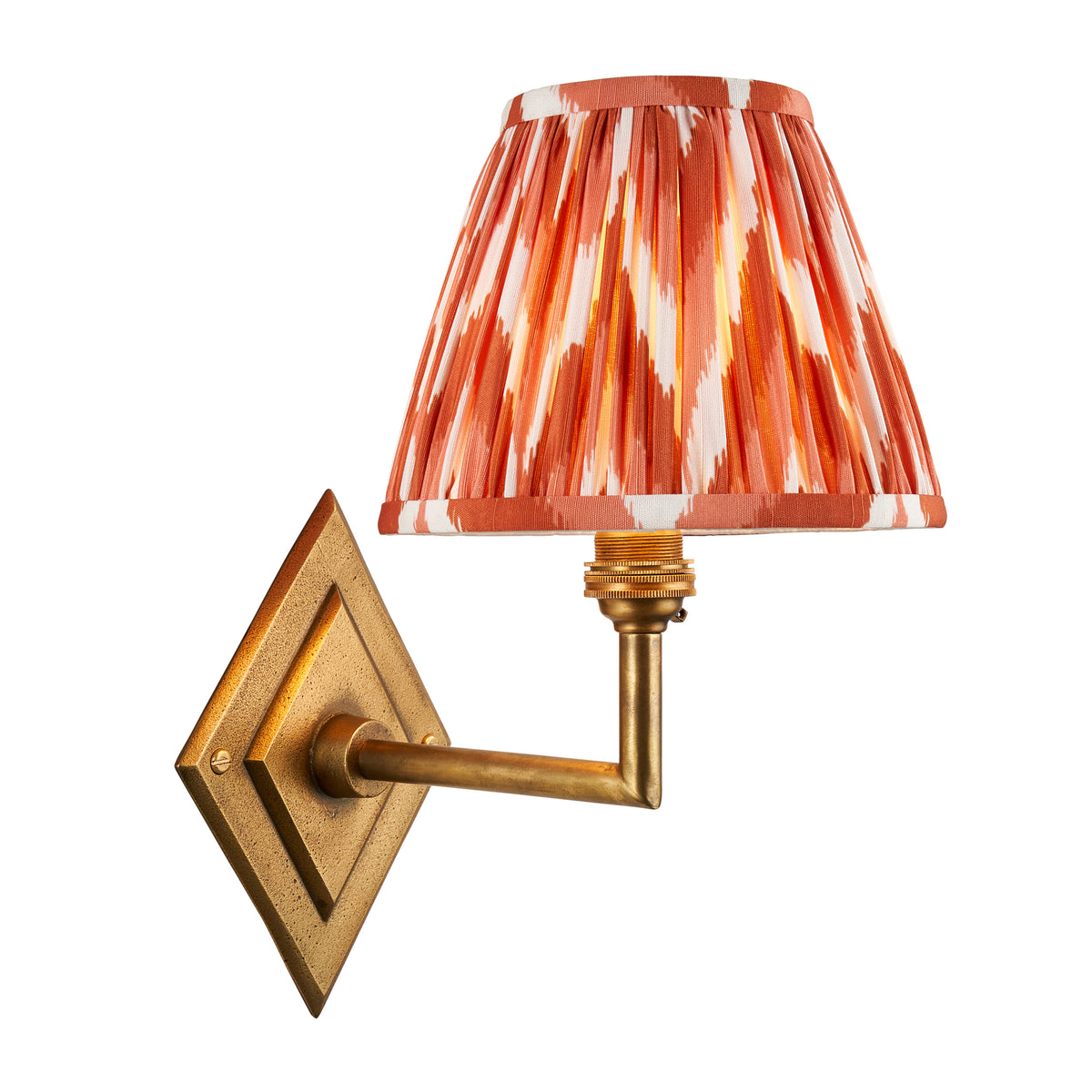 Diamond Angle antique brass wall light with a pleated orange ikat shade, softly lit