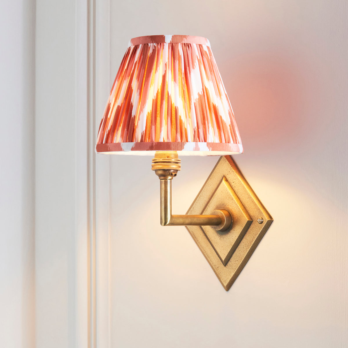 Diamond Angle brass wall light with orange ikat pleated shade, angled on white panelling