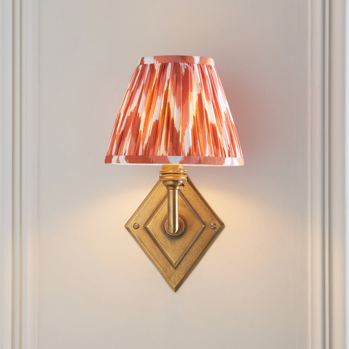 Lit Diamond Angle wall light viewed head-on, diamond brass plate below an orange ikat shade