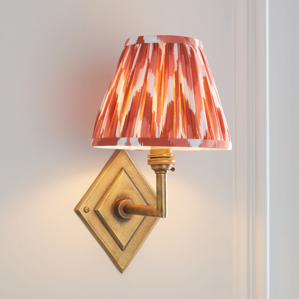 Orange ikat shade on the Diamond Angle brass wall light, lit against a white panelled wall