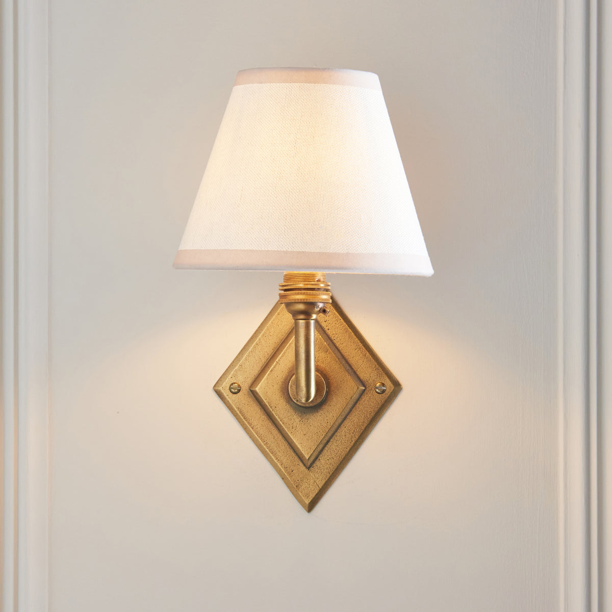 Lit Diamond Angle & Ivy wall light head-on, brass diamond backplate beneath a white shade