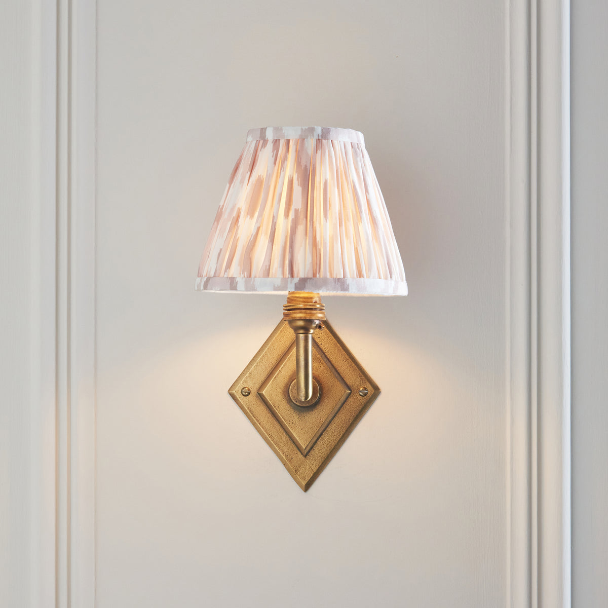 Lit Diamond Angle wall light shown head-on with brass diamond plate and natural ikat shade