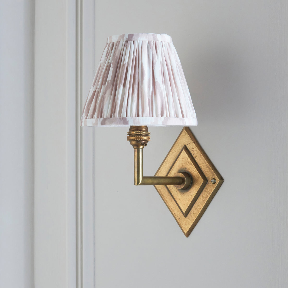 Side view of the Diamond Angle brass wall light with pale neutral pleated ikat shade
