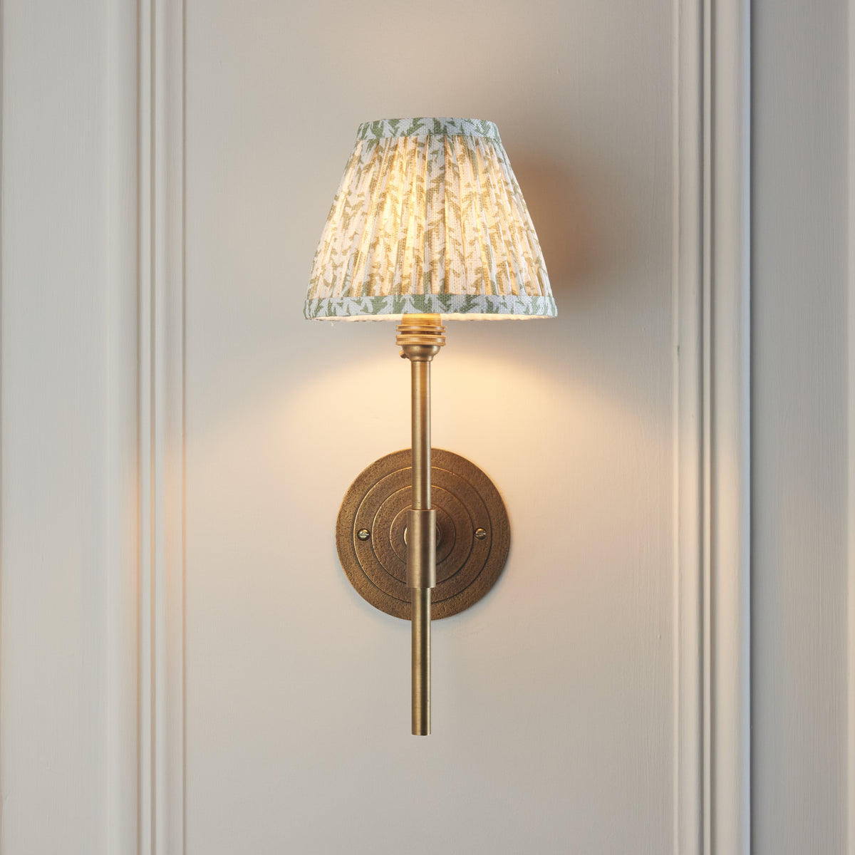 Lit Halo wall light head-on, ridged round brass backplate below a green leaf pleated shade