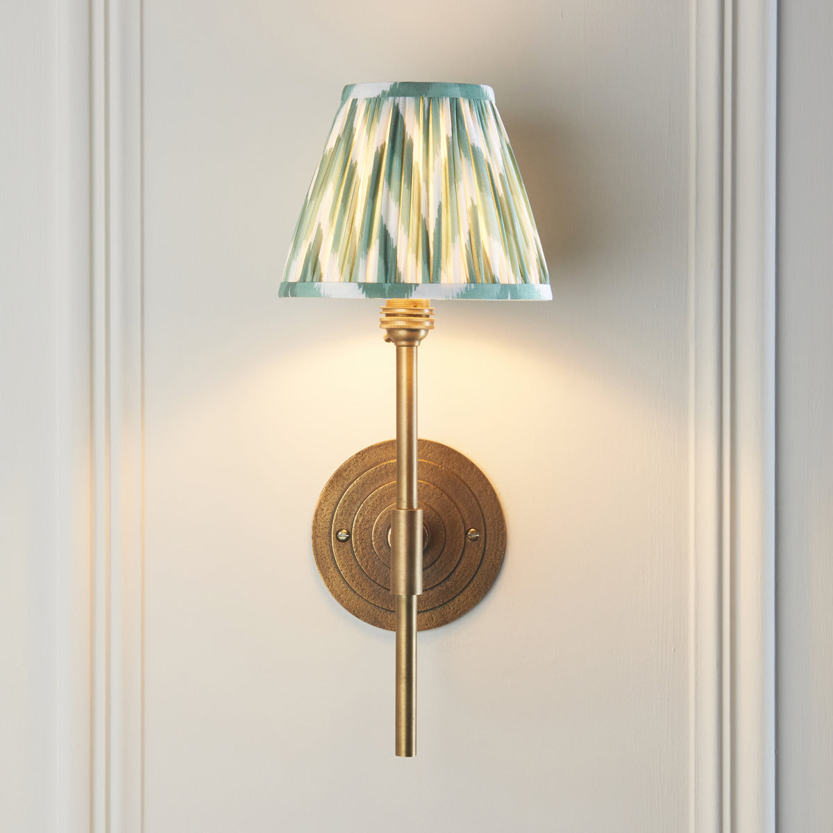 Lit Halo Tall wall light head-on, tall brass stem and round plate under a green ikat shade