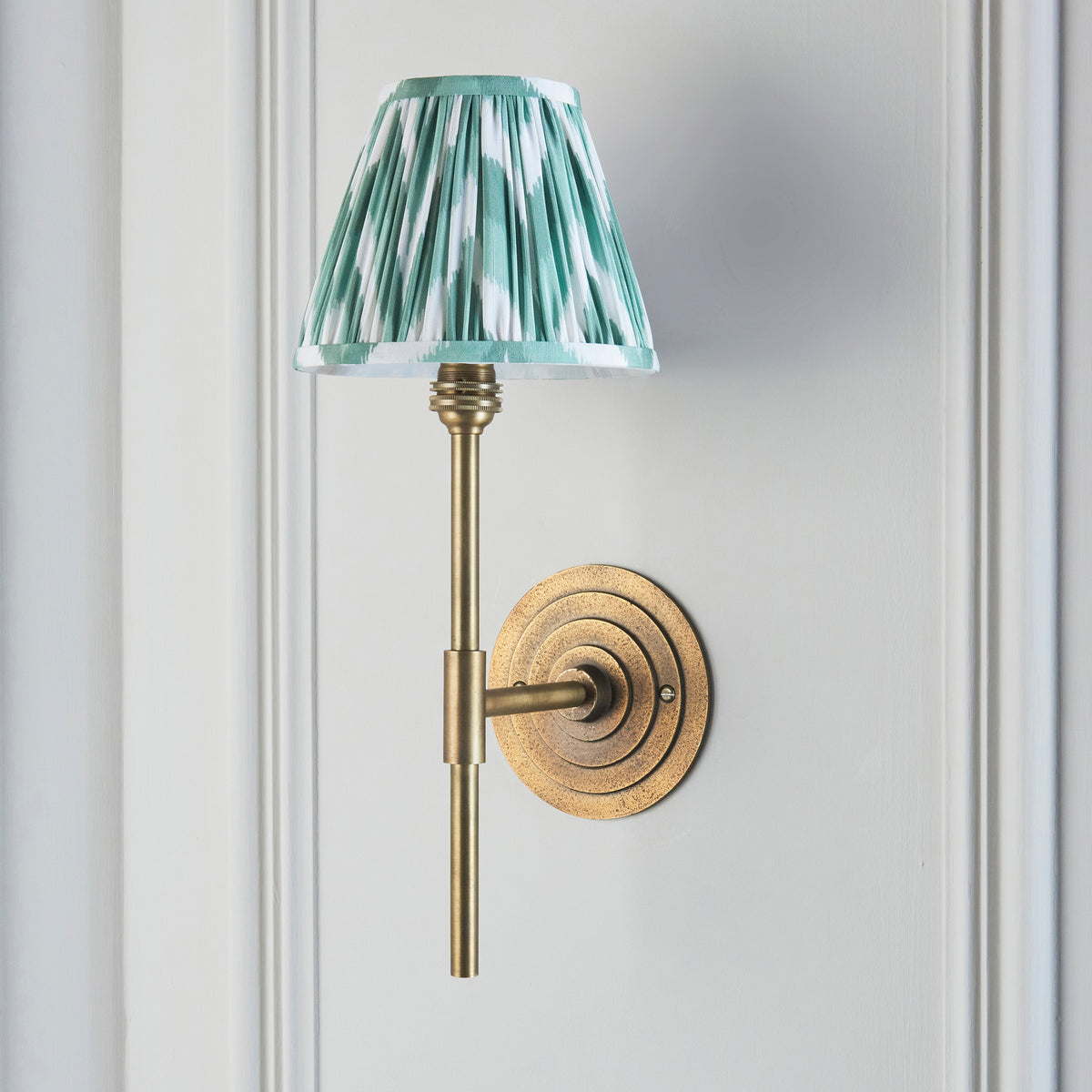 Side view of the Halo Tall brass wall light with pleated teal-green ikat shade