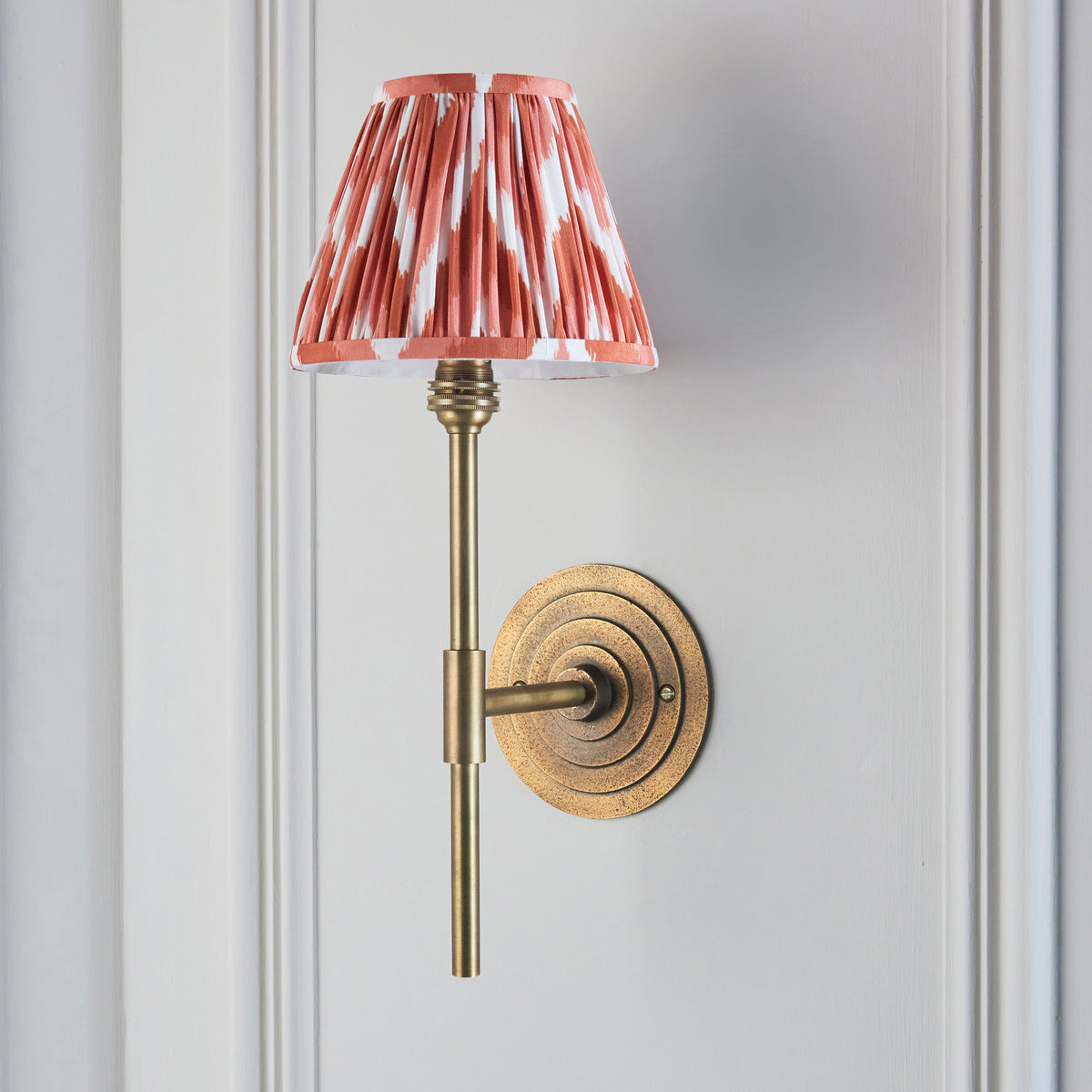 Side view of the Halo brass wall light with pleated coral-orange ikat shade