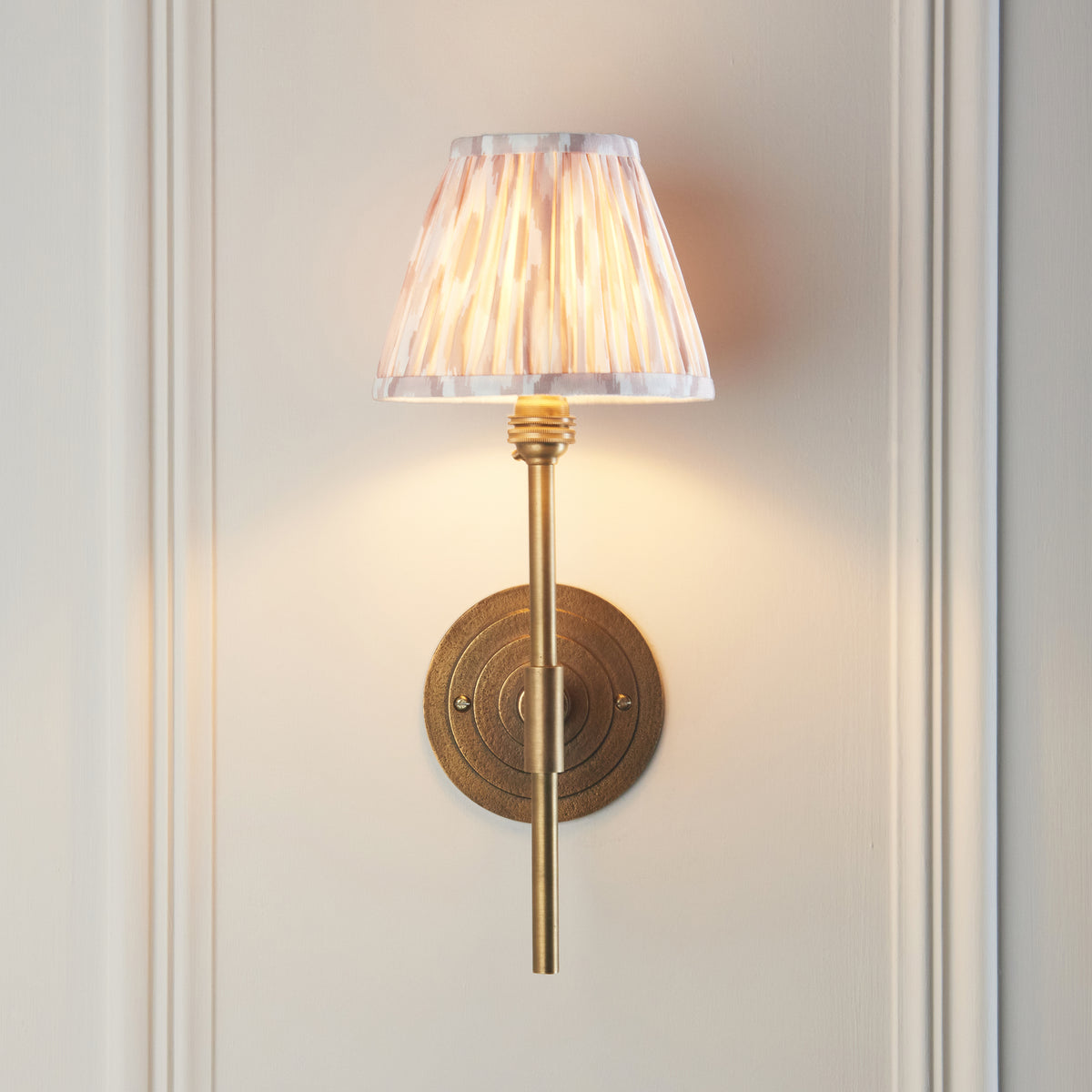 Illuminated Halo Tall wall light in antique brass with patterned ikat pleated shade on pale panelling