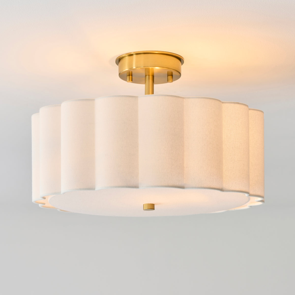 Lit Serene scalloped cream ceiling light with brushed aged brass ceiling plate, seen from below